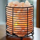 Cylindrical Himalayan salt lamp with iron frame emitting warm light for relaxation and air purification