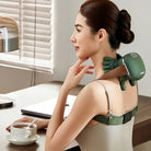 Woman using a green massage device on her back in a home office setting.