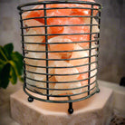 Cylindrical Himalayan salt lamp with iron frame emitting warm light for relaxation and air purification